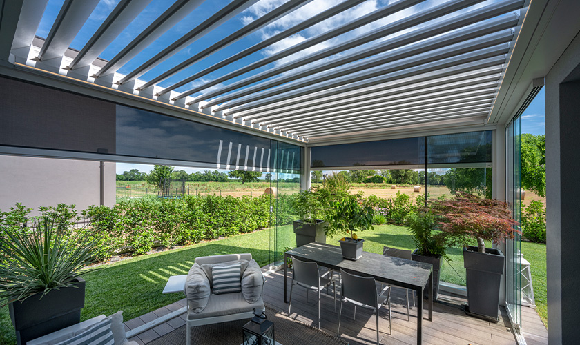 Überdachte Terrasse mit modernen Möbeln, Pflanzen, und Gartenblick unter blauem Himmel.