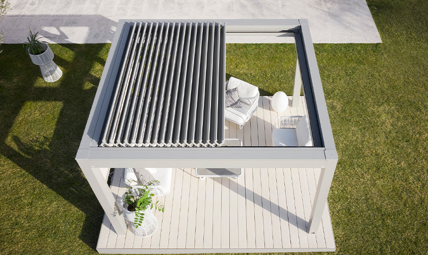 Moderne, offene Pergola auf Terrasse mit weißen Möbeln und Pflanzen, Vogelperspektive.