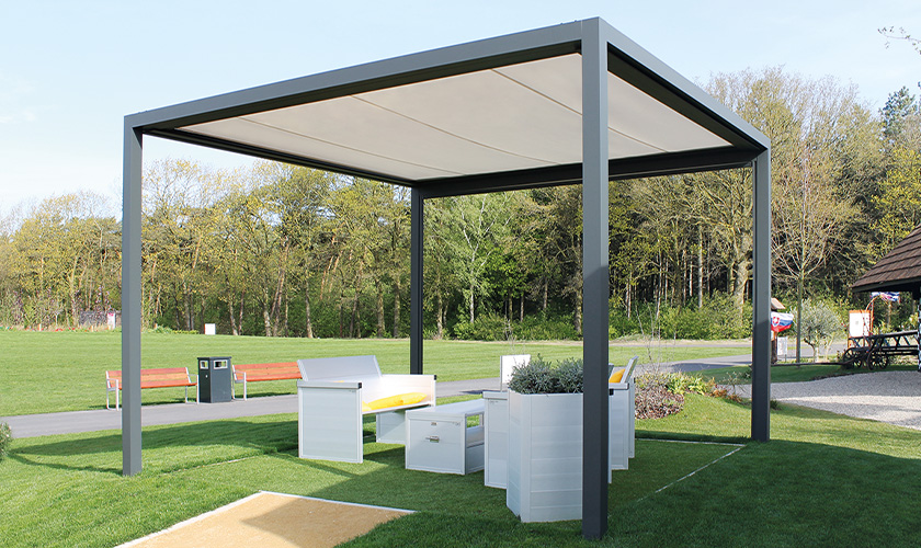 Freistehender moderner Pavillon mit weißen Sitzmöbeln im Grünen, Sonnendach und Bäume im Hintergrund.