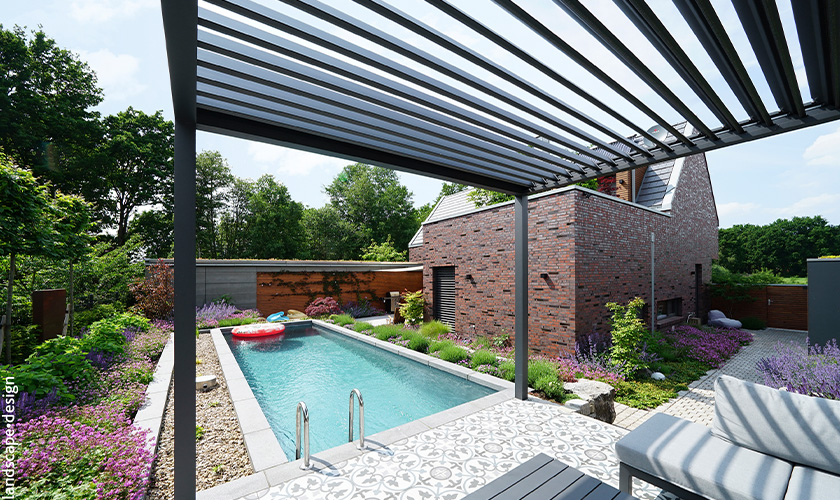 Ein moderner Garten mit Pool, umgeben von Pflanzen, und einem Backsteingebäude im Hintergrund.