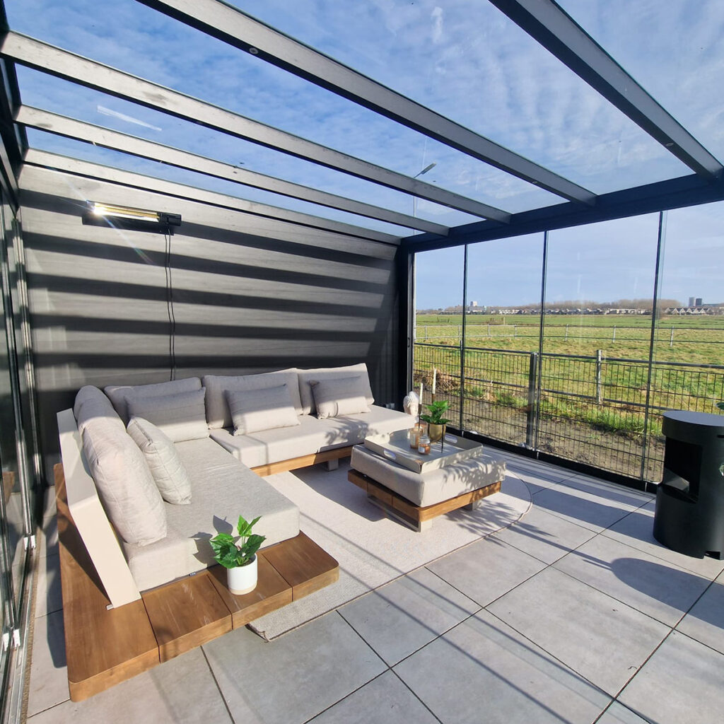 Eine moderne Veranda mit Sofas, Pflanzen, Glasdach, Blick auf Felder, neutralen Farben.