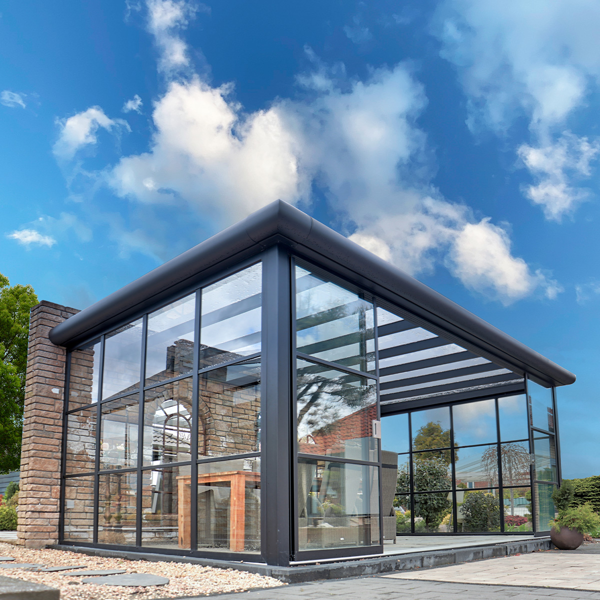 Modernes Glashaus mit schwarzem Rahmen vor blauem Himmel und Wolken.