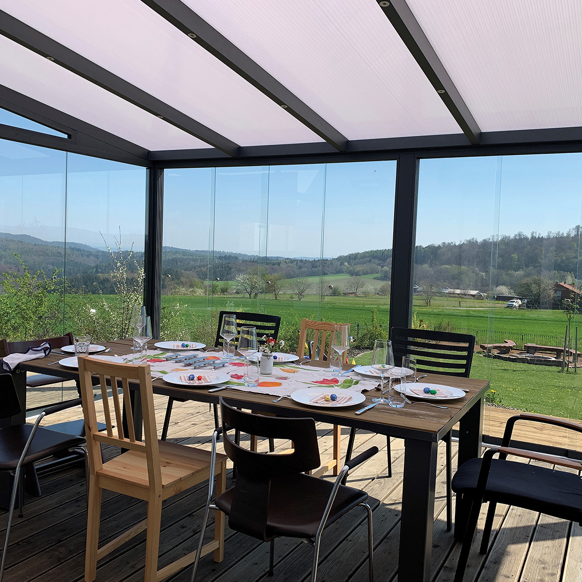 Ein Tisch auf einer Terrasse, gedeckt mit weißen Tellern und Gläsern, ländliche Aussicht im Hintergrund.
