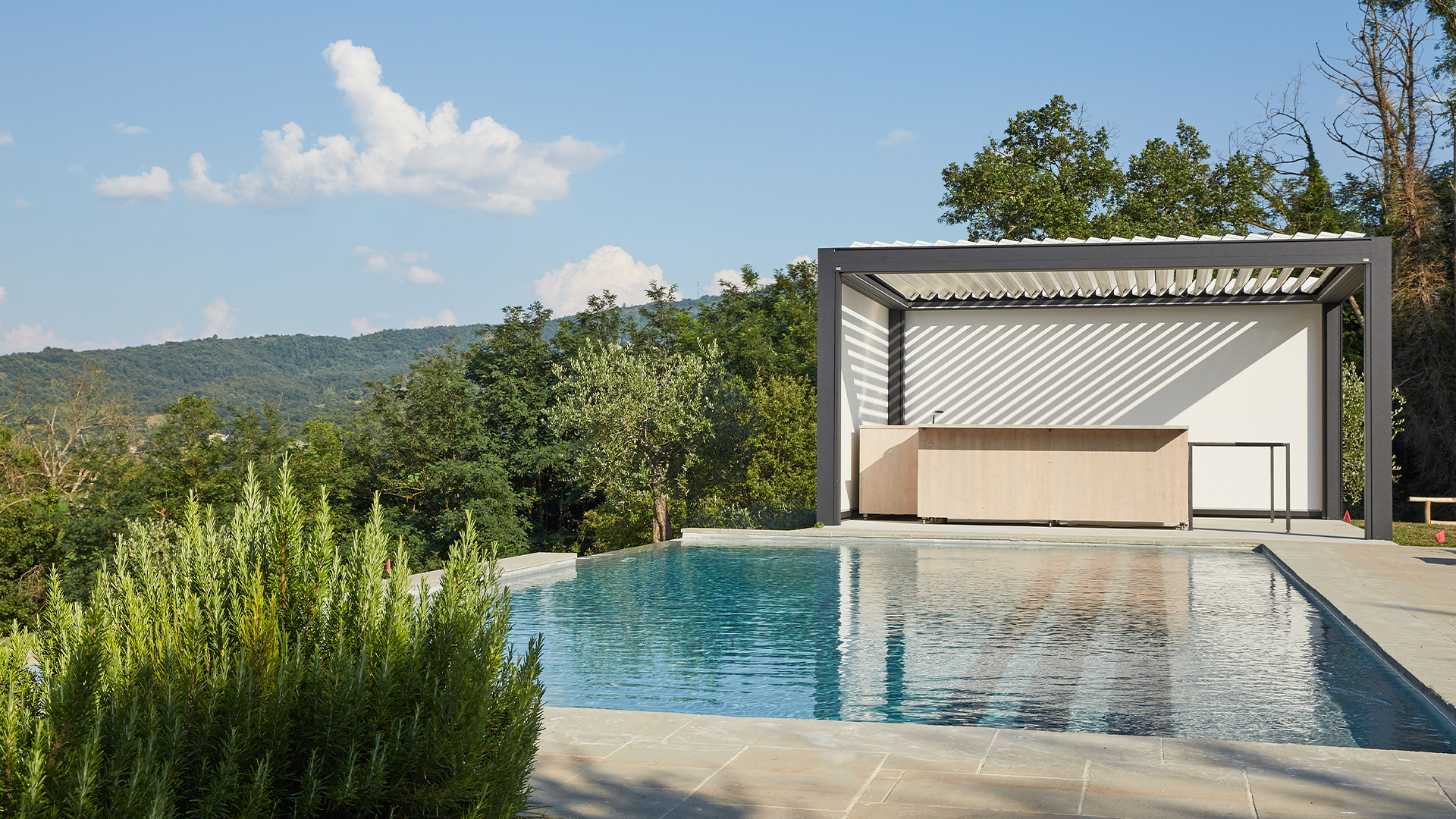 Ein moderner Pool mit Pavillon, umgeben von üppigem Grün, unter blauem Himmel.