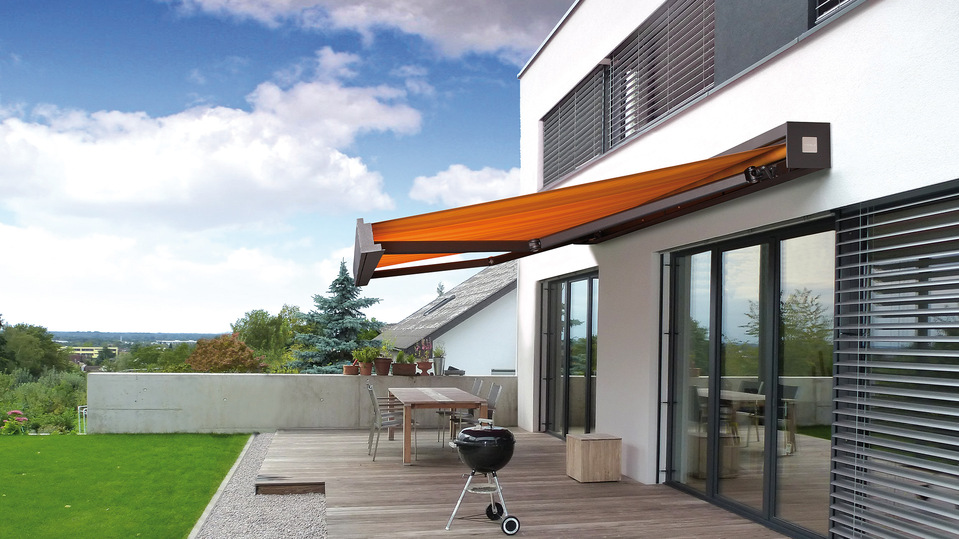 Moderne Terrasse mit orangefarbener Markise, Tisch, Stühlen und Grill, grüner Rasen im Vordergrund.