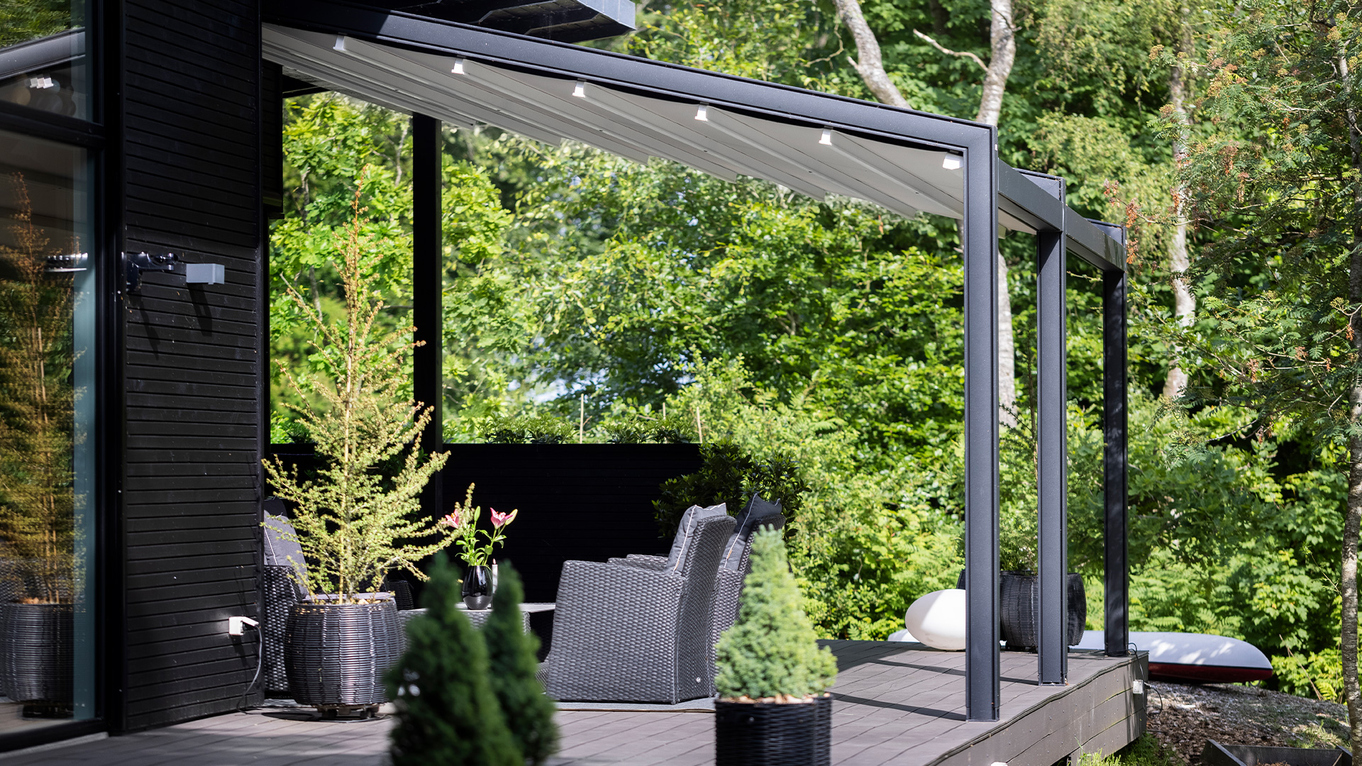 Moderne Terrasse mit schwarzem Mobiliar, umgeben von üppigem Grün; friedliche Atmosphäre.